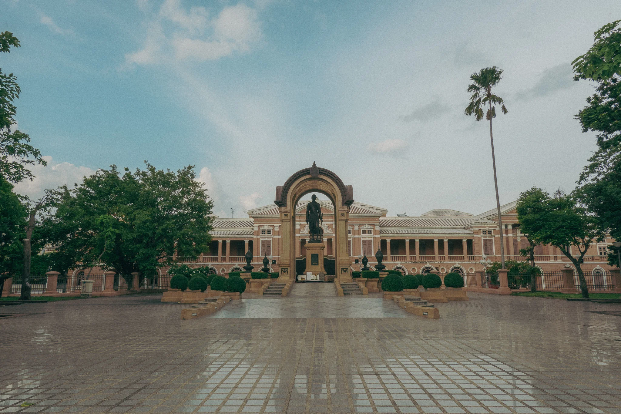 Vast tan state building with  green palm trees and blue skies in the background