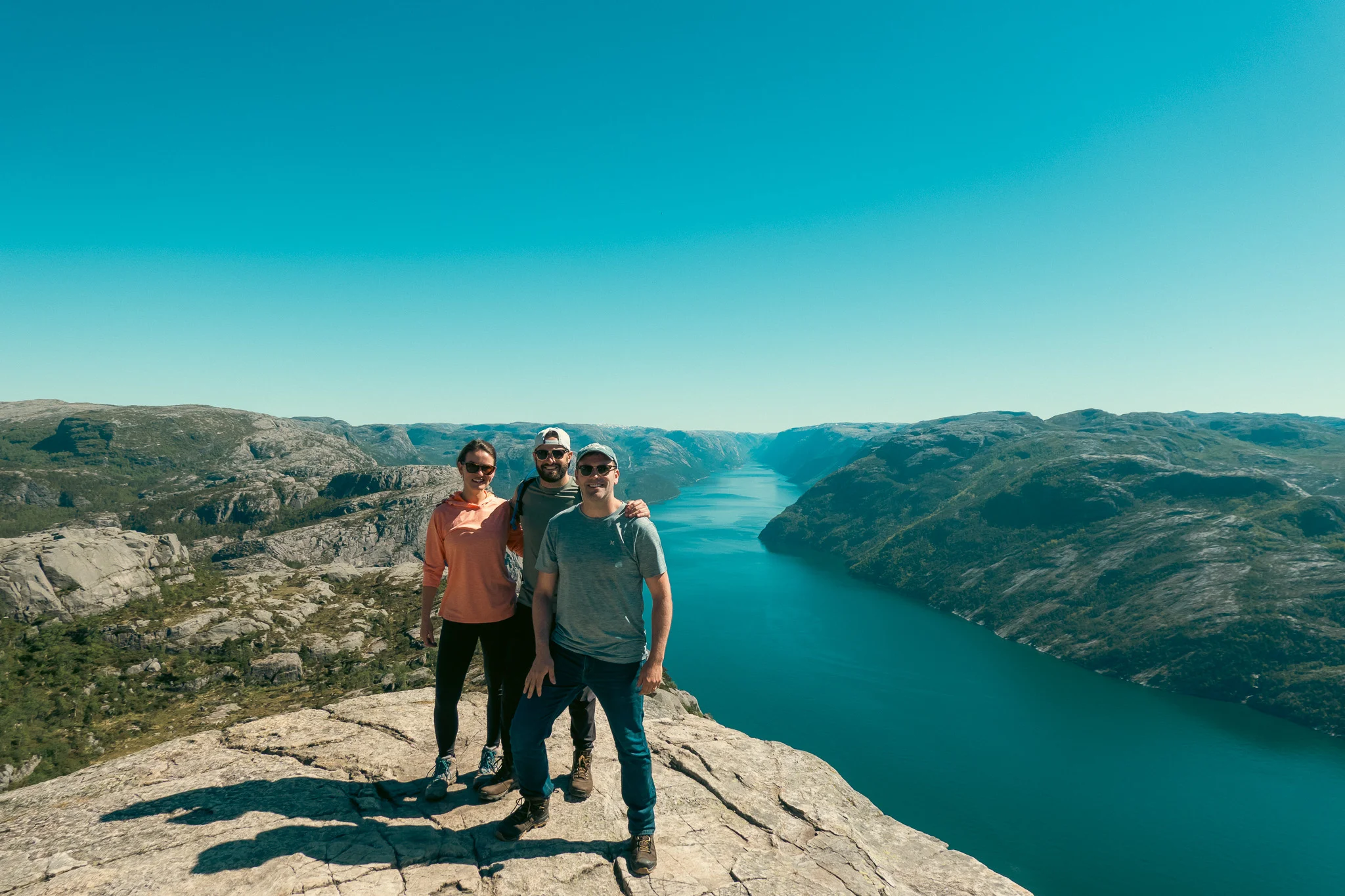 Two men and a woman posing at Pulpit Rock with the fjord and mountains in the background