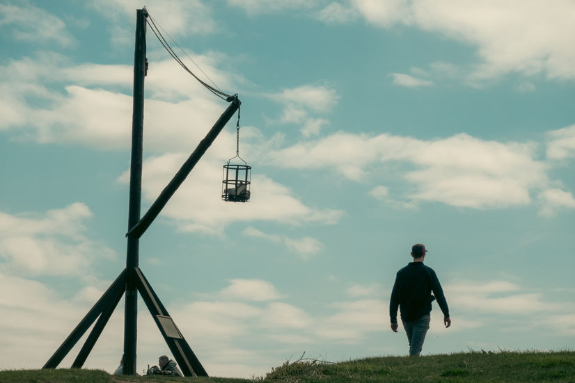 A wooden stand with a metal cage lantern and a man walking past in the Kullaberg national preserve