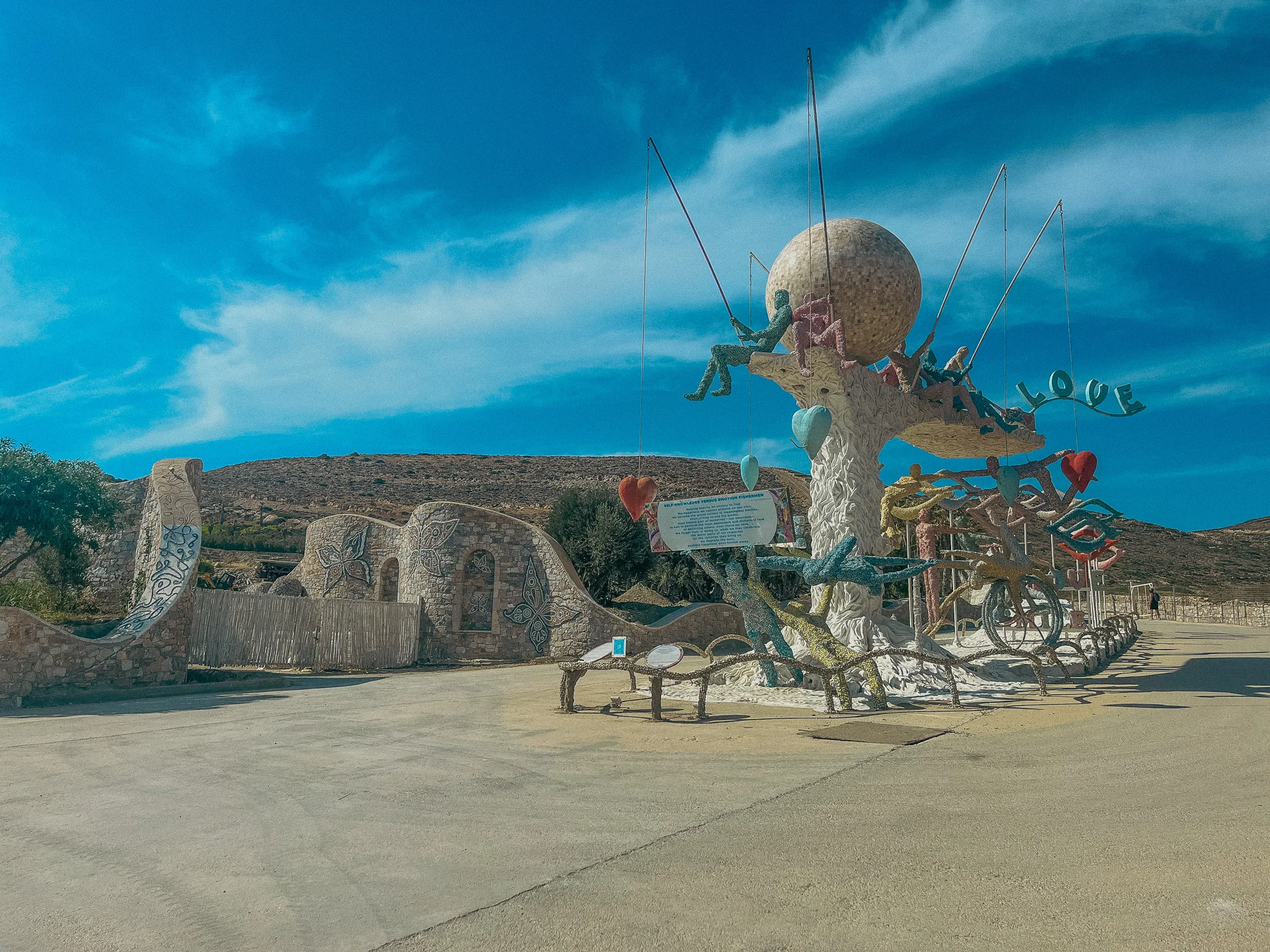 A tall abstract art piece on cement with blue sky in the background
