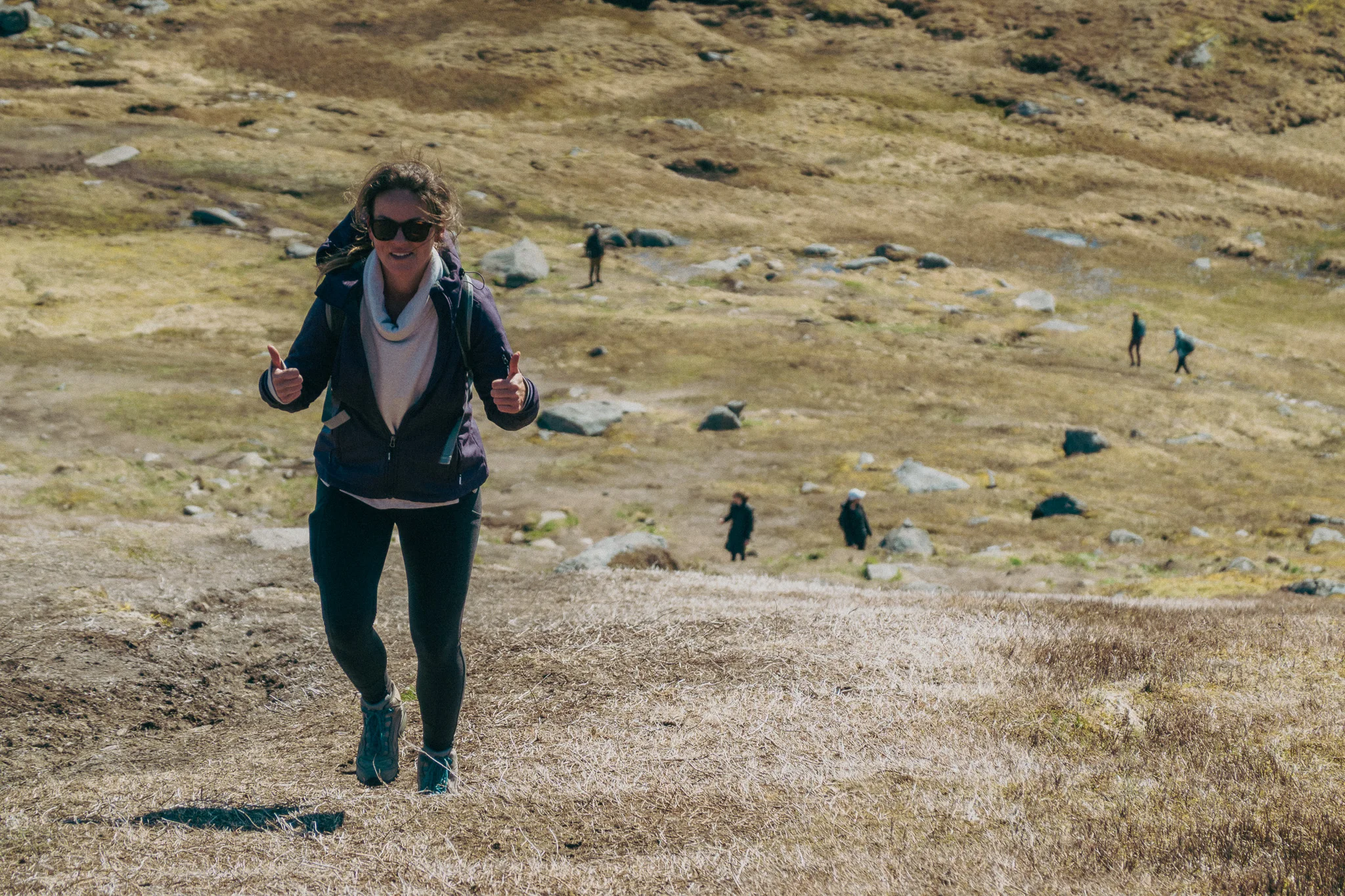 A female hiker in a purple jacket poses with two thumbs up on a steep dirt trail