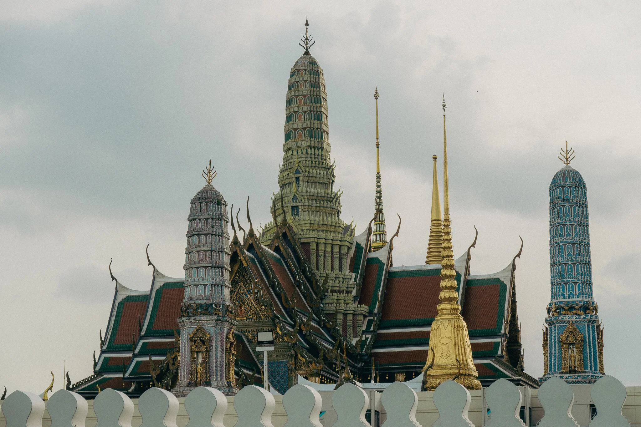 Traditional Thai temple with gold red and white structures and cloudy skies in the background