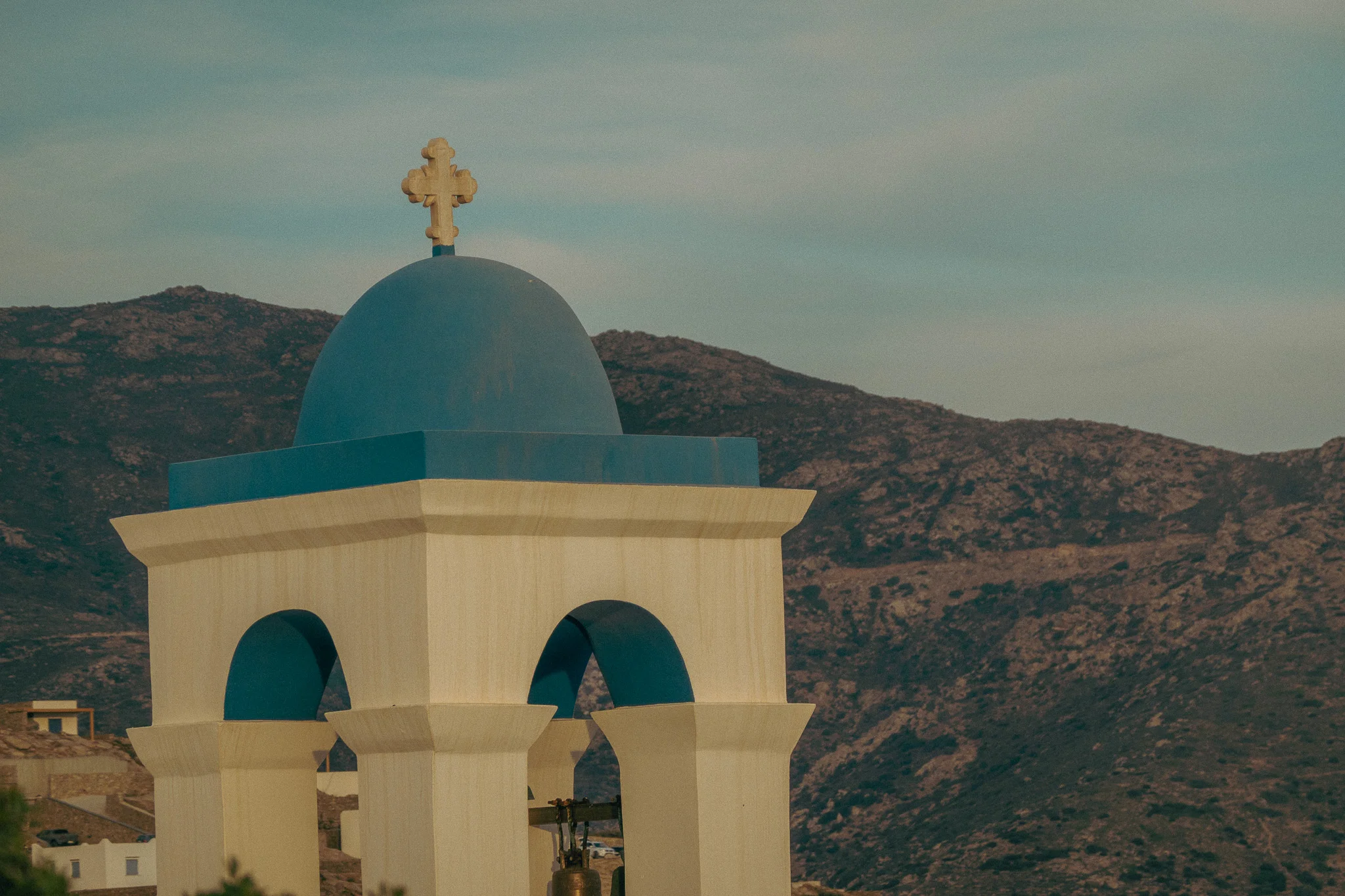 The top of a white a blue chapel with mountains in the background at dusk