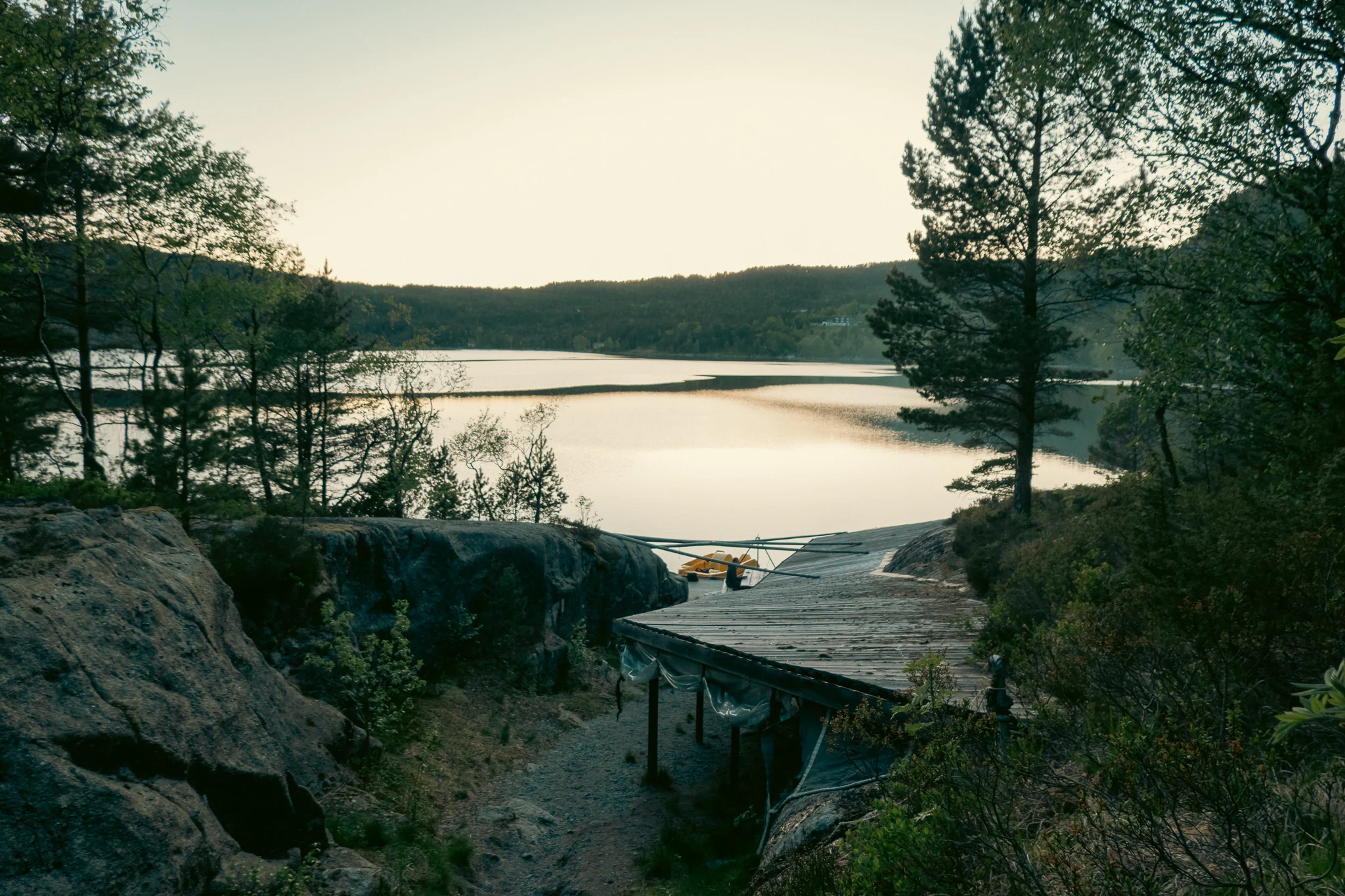 A wooden campsite shelter lined by trees with a lake and mountains in the background at sunset.