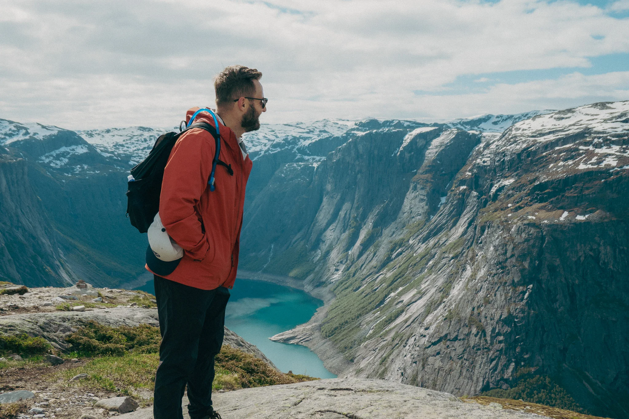 Adult male poses in front of scenic landscape and snowcapped mountains on the Trolltunga trail in Norway