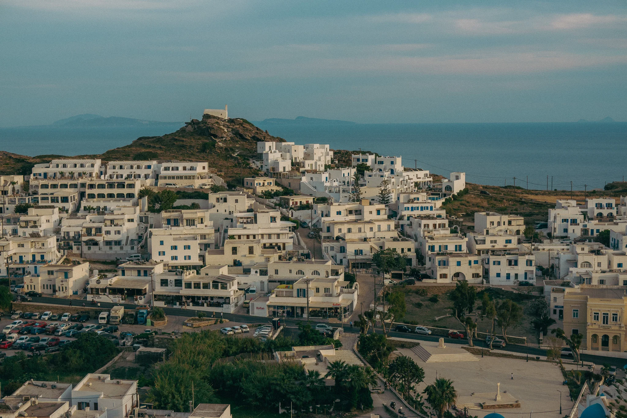 A small chapel perched atop a hill surrounded by white building and ocean in the background