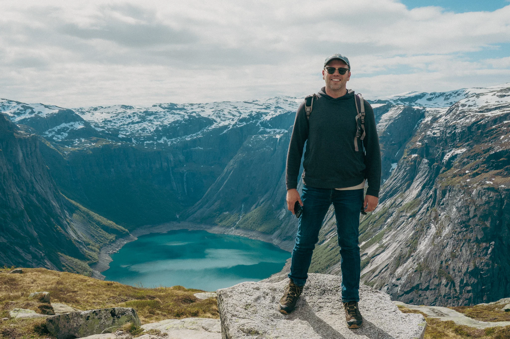 Adult male poses in front of scenic landscape and snowcapped mountains on the Trolltunga trail in Norway