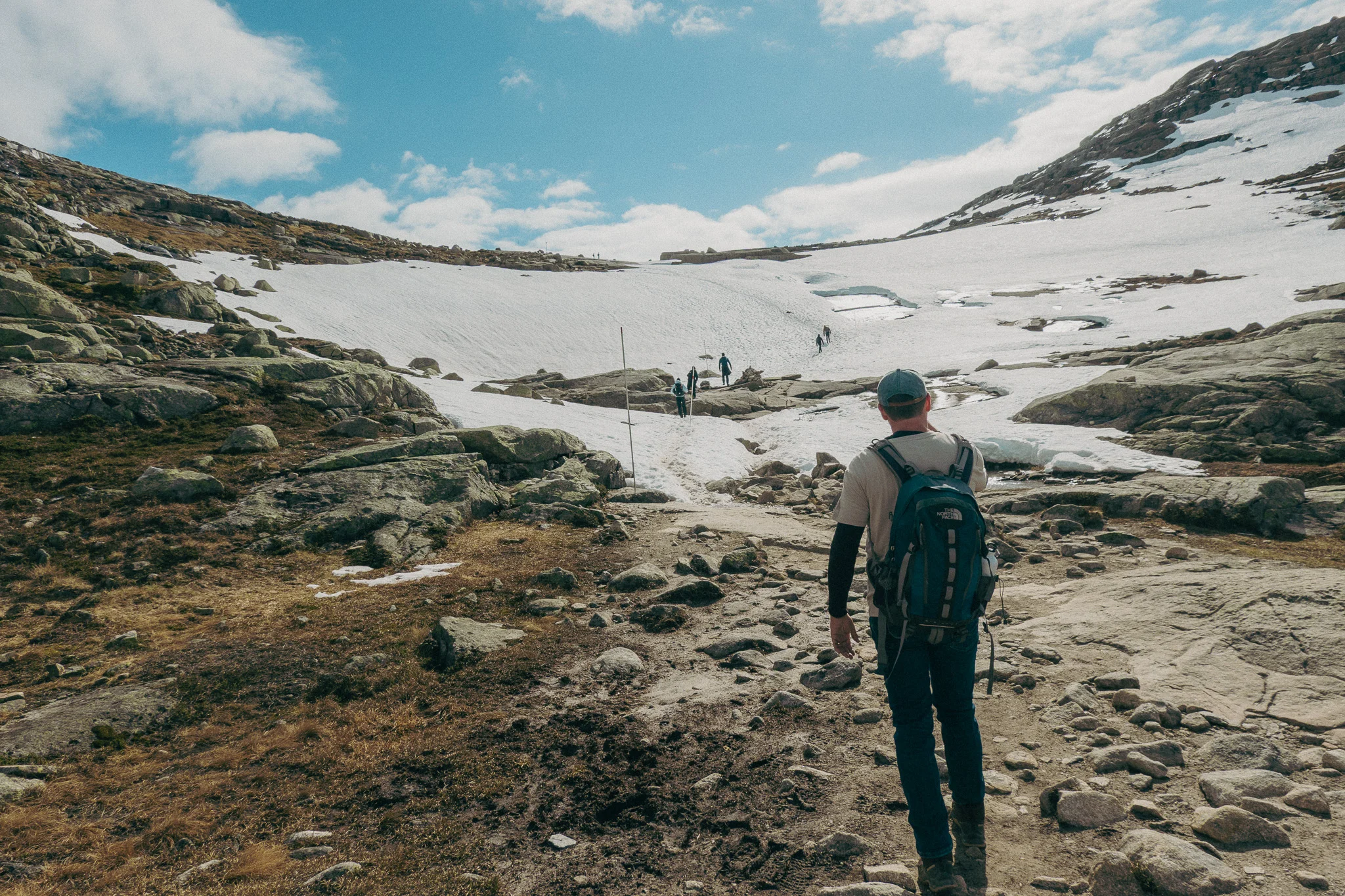 Adult hiking on rock trail with snow and blue skies in the background on the Trolltunga trail in Norway