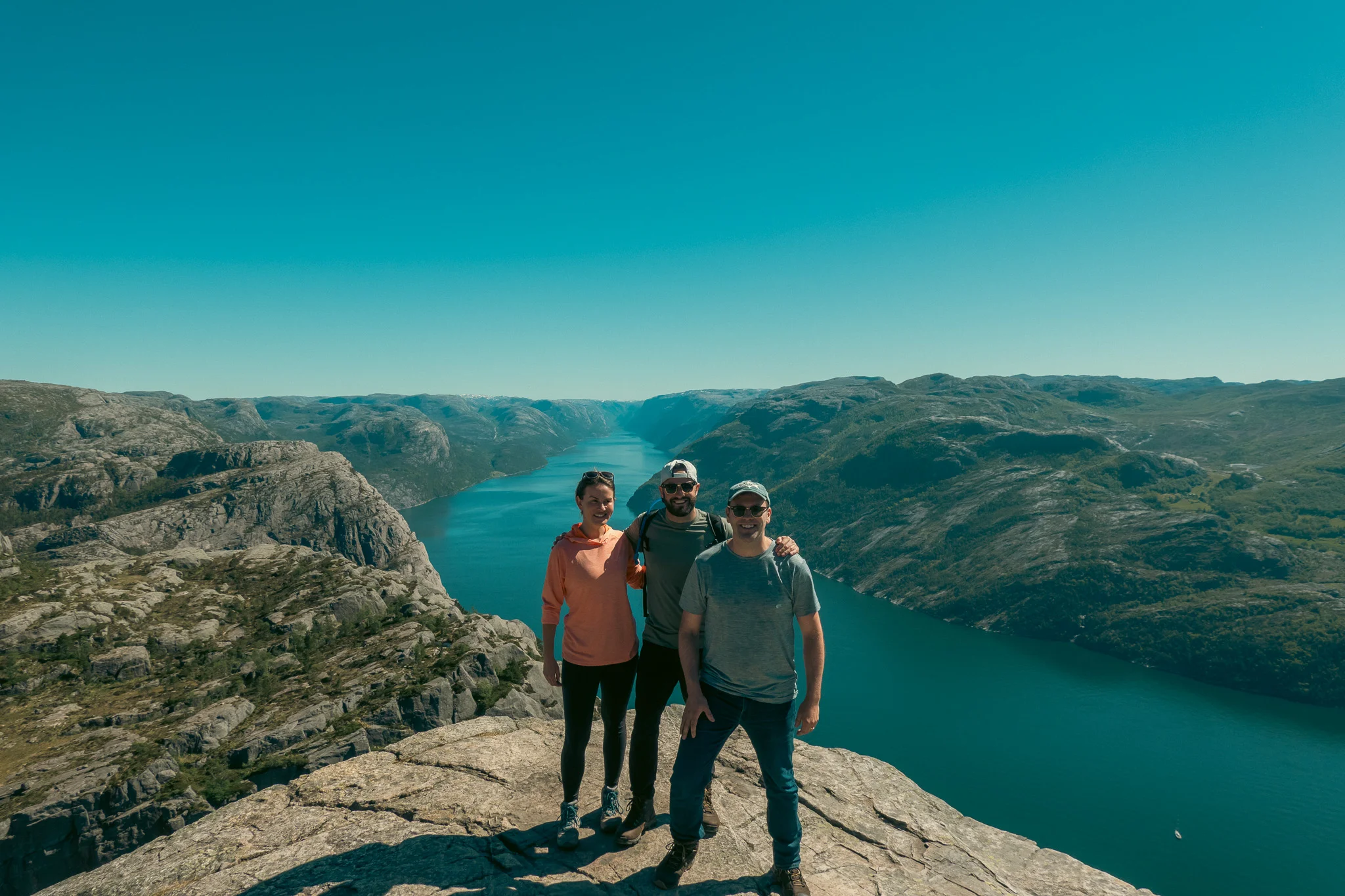 Two men and a woman posing at Pulpit Rock with the fjord and mountains in the background