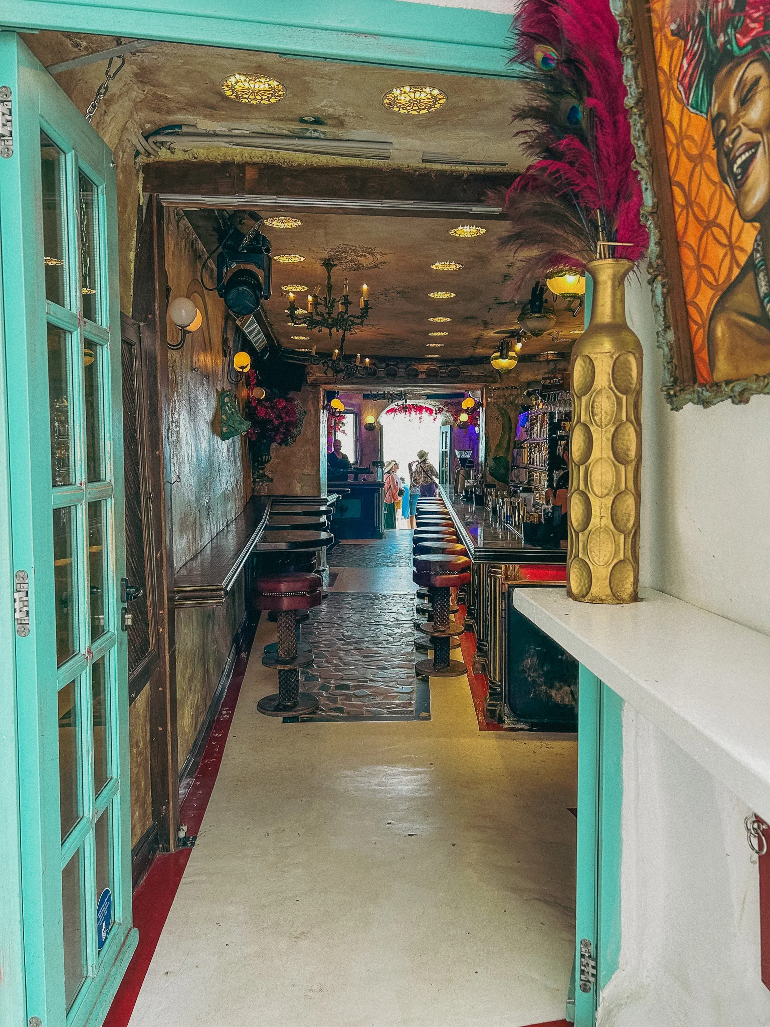 Narrow entryway to a shotgun style bar with a teal paint on the entry way door and a patio leading to the water in the background