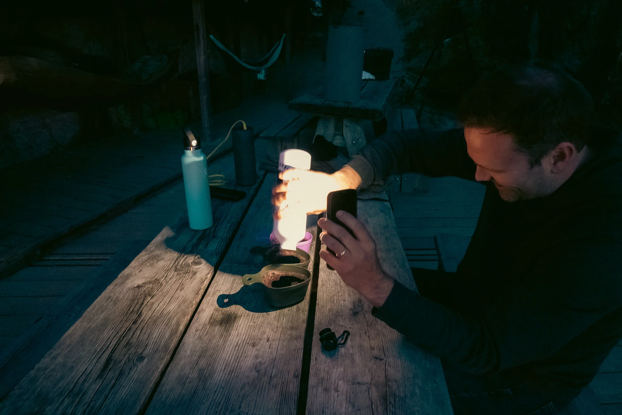 A man pouring a drink from a water bottle into a large measuring cup at a picnic table at night.