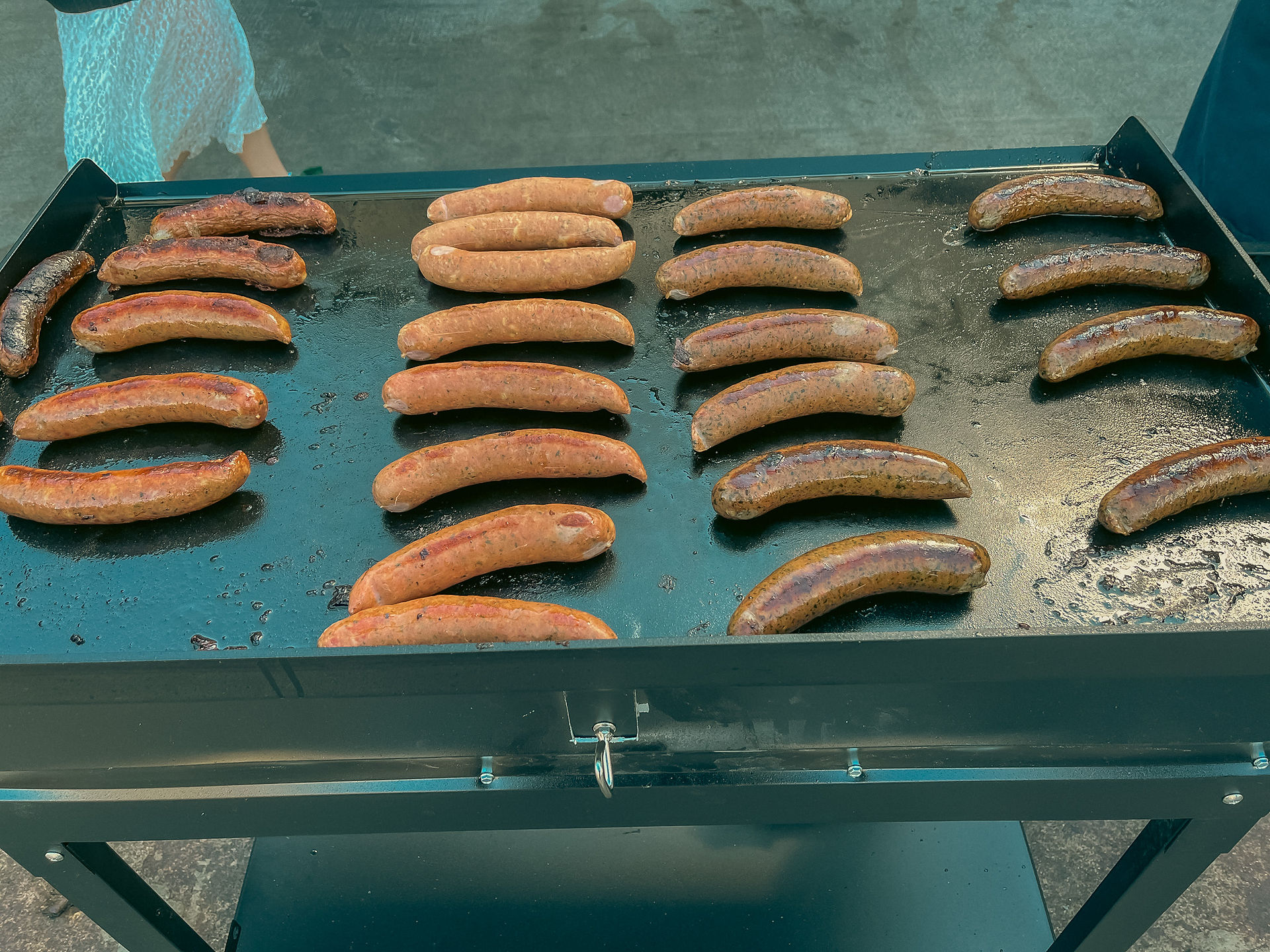 Sausages being cooked on a griddle at Broens Street Food market People eating at picnic tables in front of a food stand at Broens Street Food in Copenhagen, Denmark