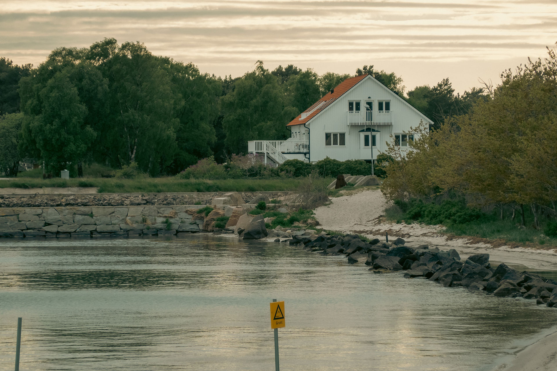 A house on the water with nice green trees to the left at Höllviken beach in Sweden