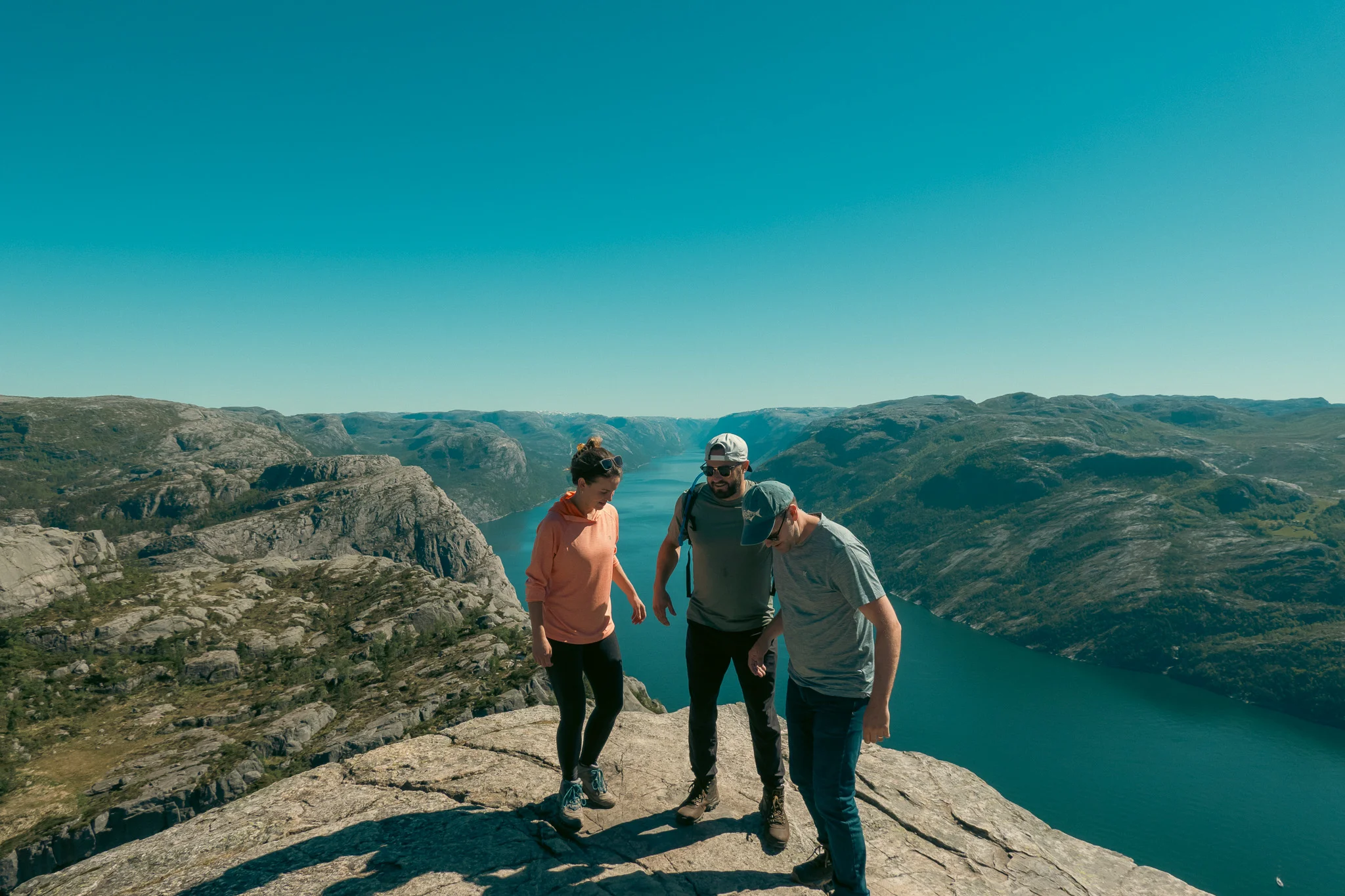 Two men and a woman approach the ledge at Pulpit Rock with the fjord and mountains in the background
