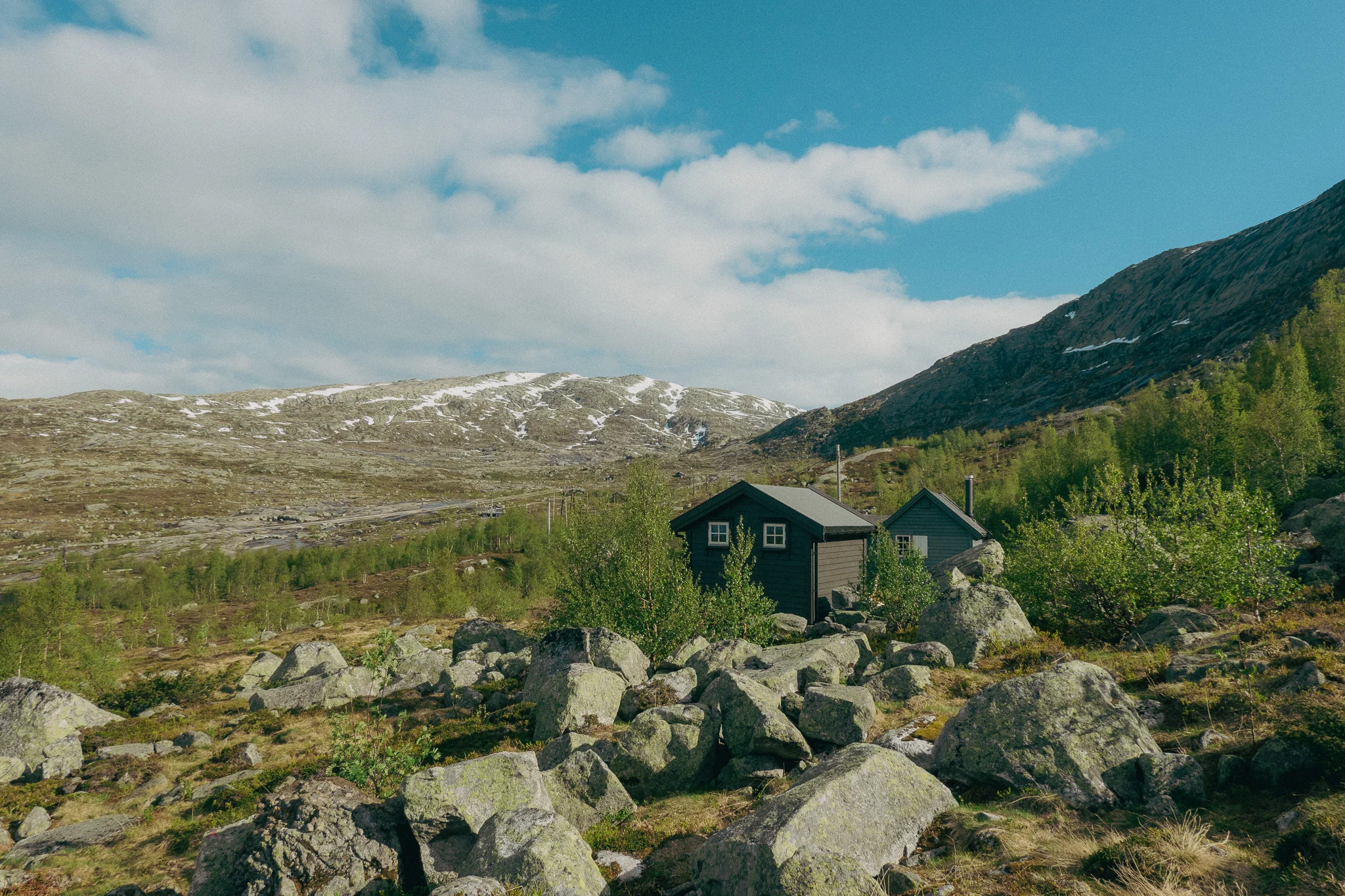 A survival cabin anchored to rocks surrounded by green plants on the Trolltunga trail in Norway