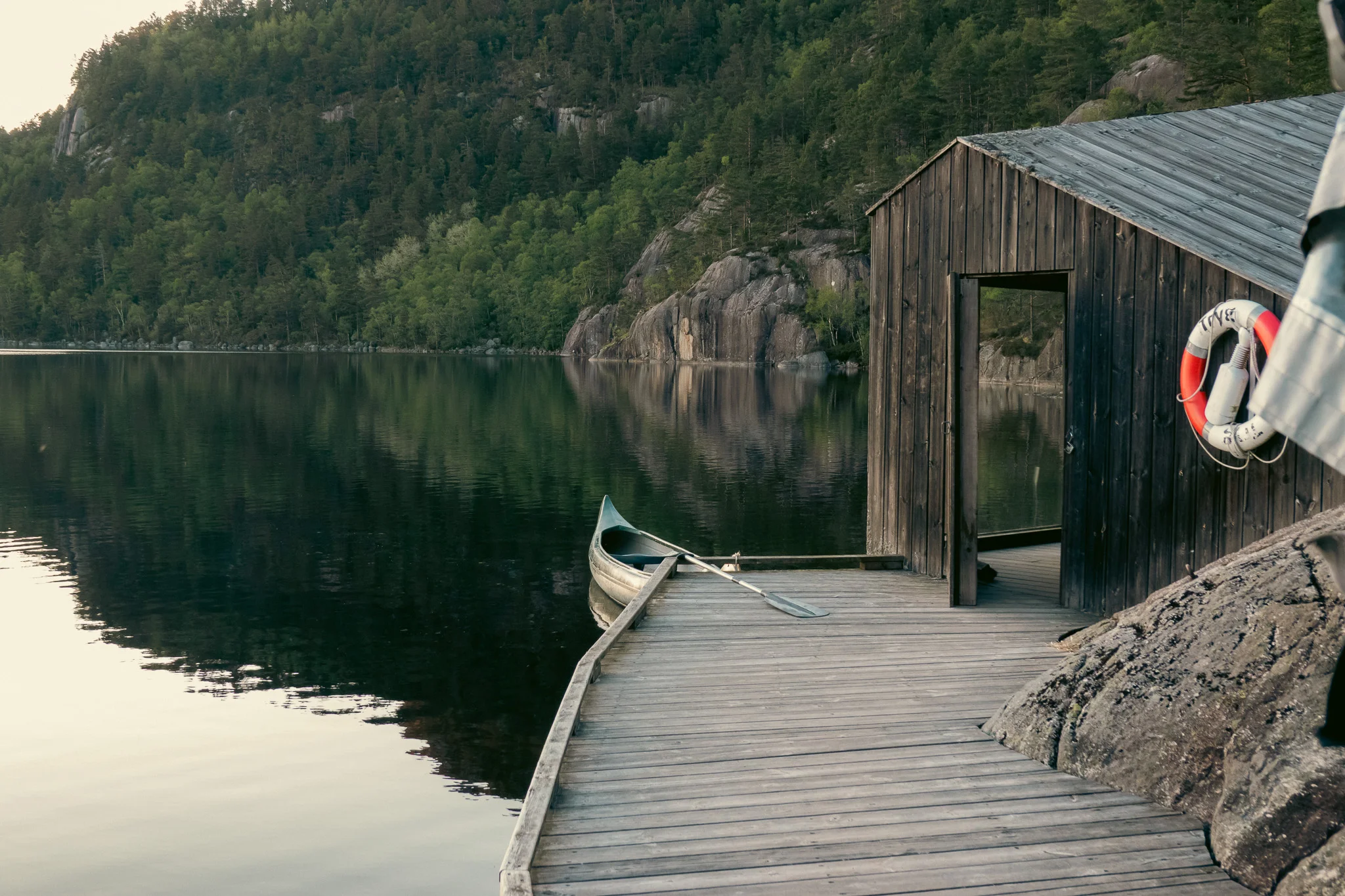 A wooden dock and shed alongside a lake with a canoe tied to the dock and mountains in the background.