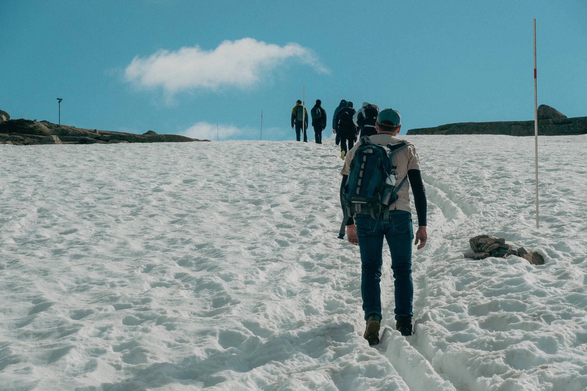 A line of adults hiking through snow surrounded by rocks and blue sky in the background on the Trolltunga trail in Norway