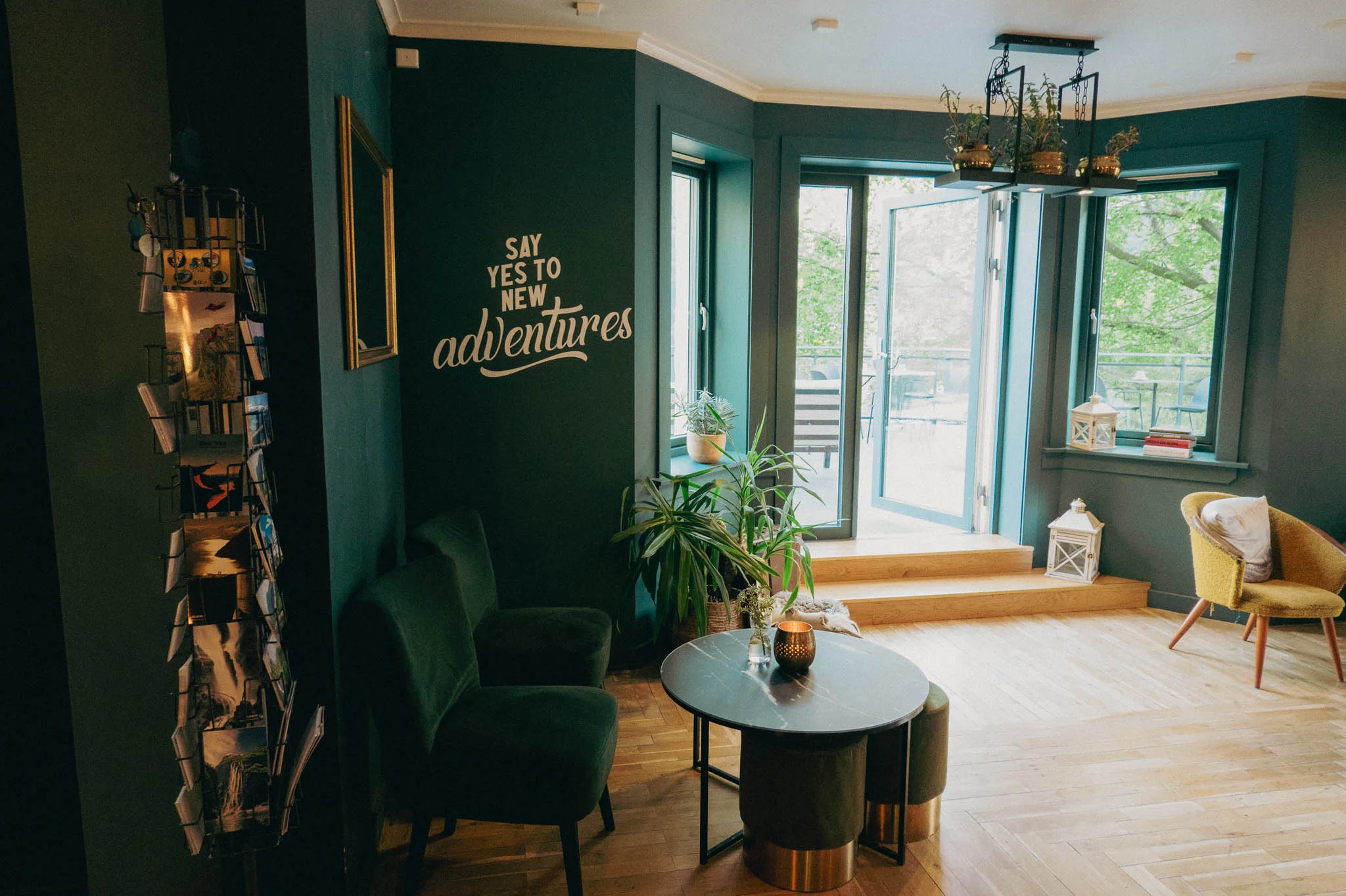 Hotel lobby with green chairs, a small table with a candle on it, and typography on the wall that reads "say yes to new adventures"