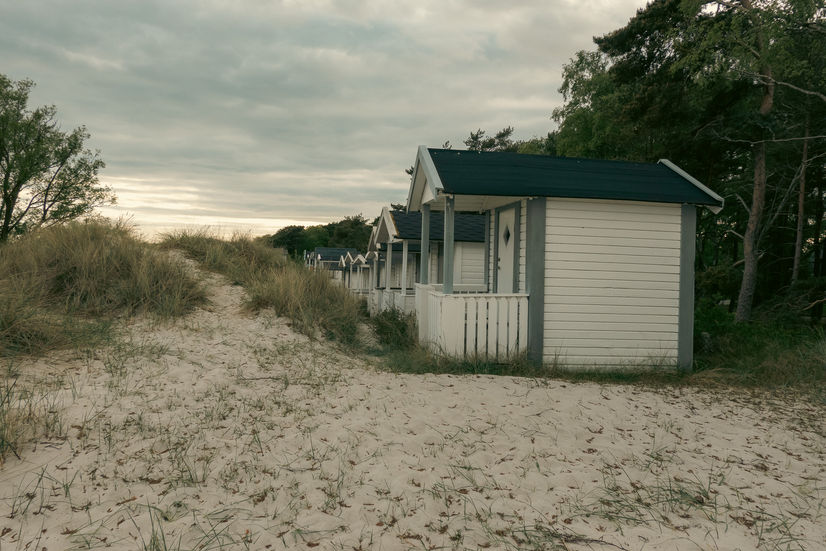Beach cottages lined up behind the beach grass and sand dunes at sunset at Höllviken beach in Sweden