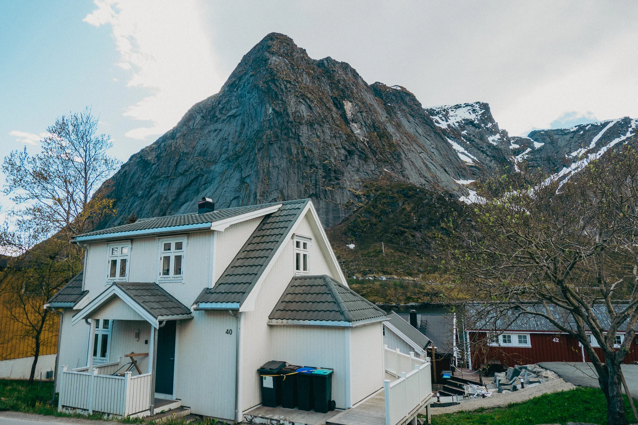 A small white cottage with a jagged, rocky, snow-capped mountain in the background