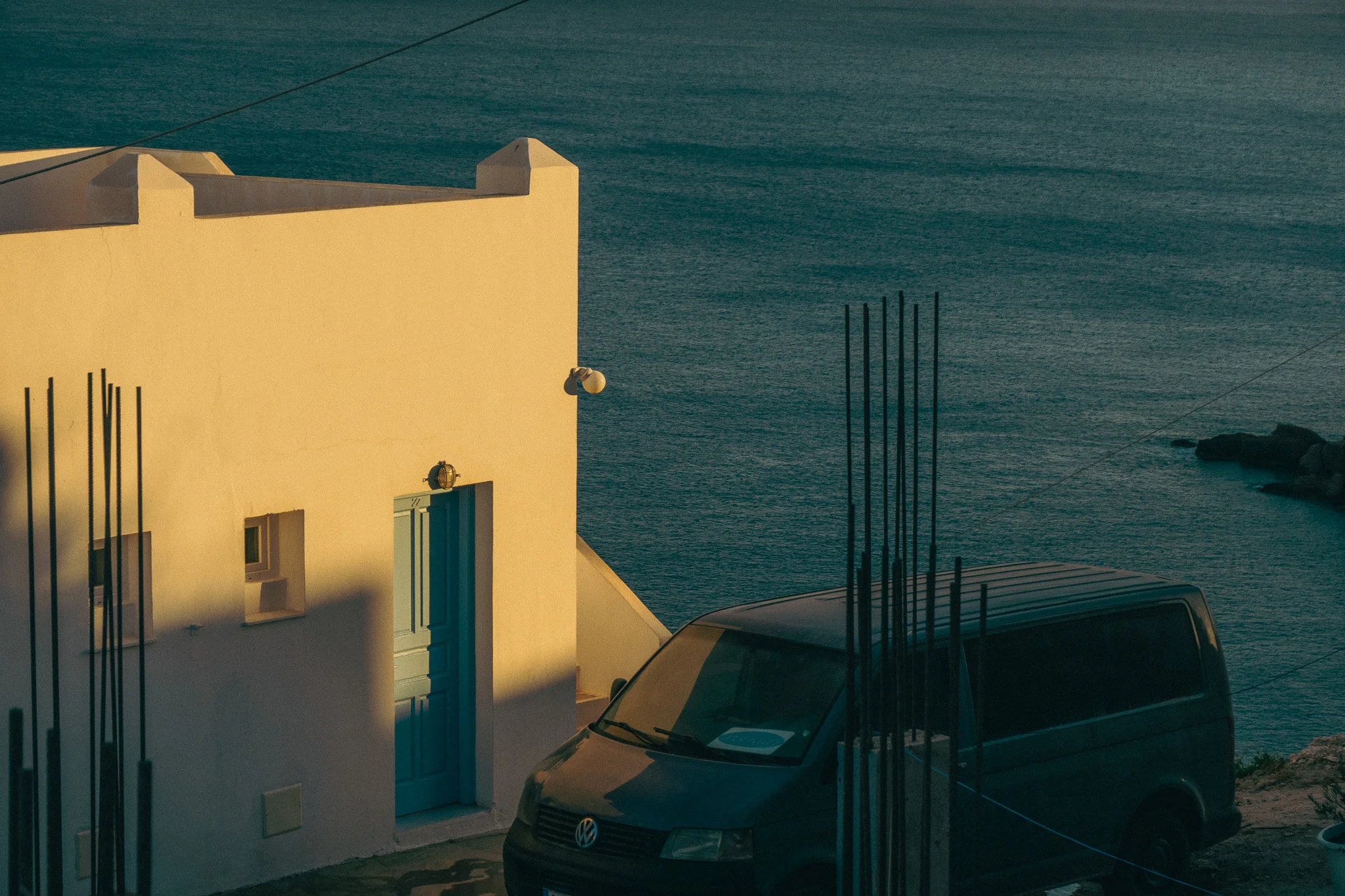A white building with a blue door and a van parked outside overlooking the water