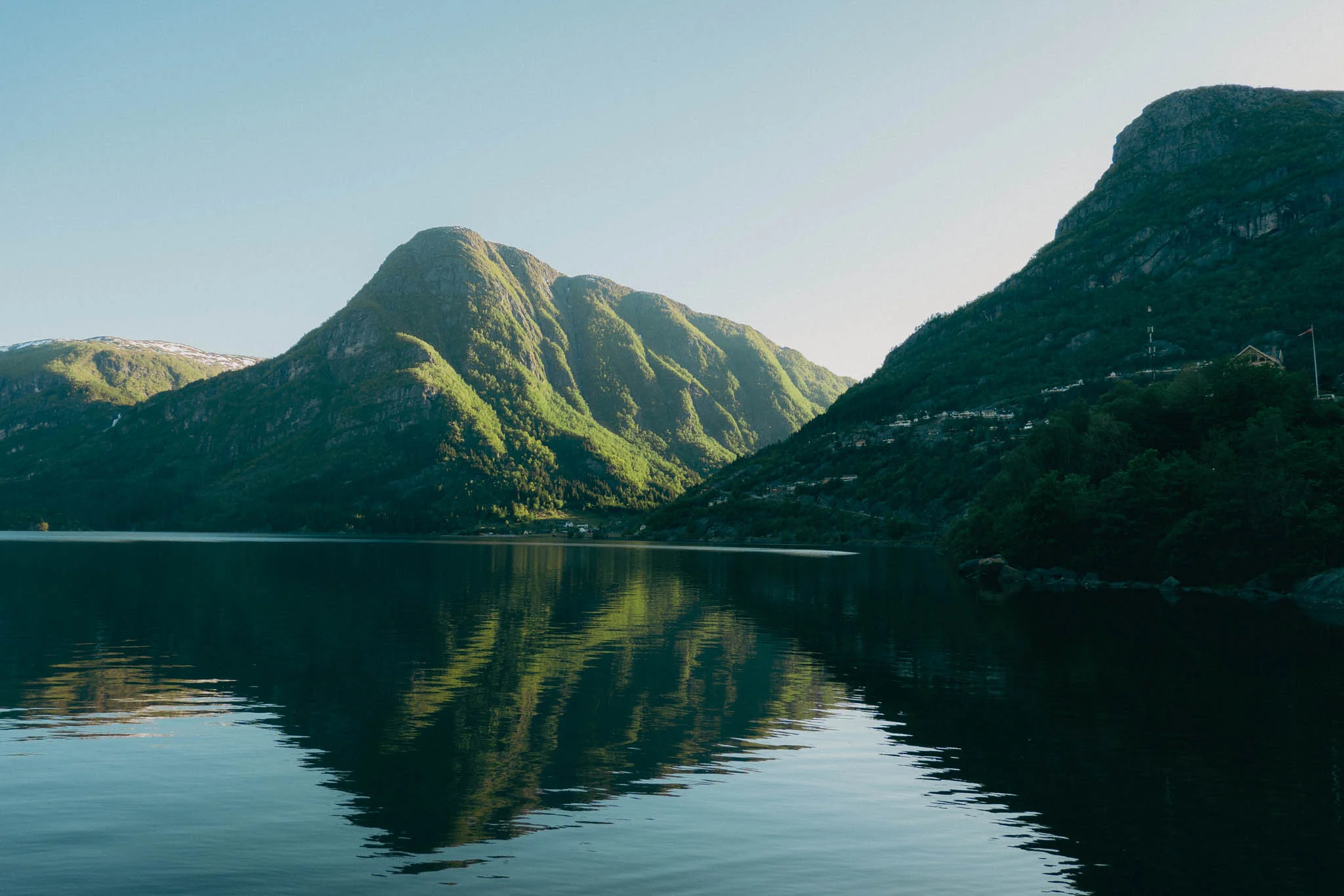 Clear fjord water reflecting the green sunlit mountains in the background