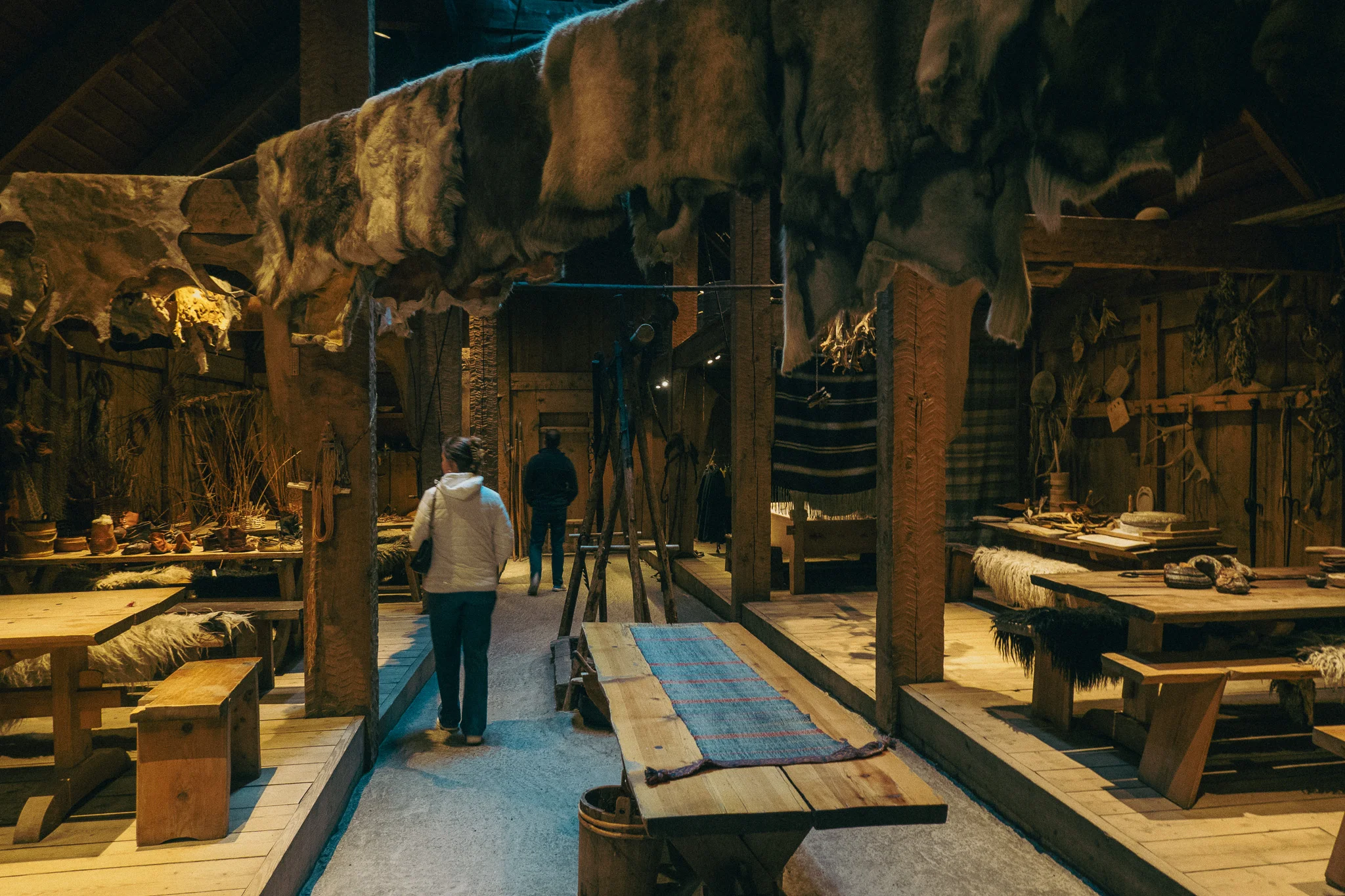 A room in Lofotr Viking Museum with tables and fur hides hanging from the rafters