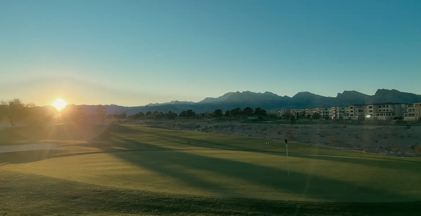 Sunset at Angel Park Golf Course with the putting green in the foreground and sun setting over the desert mountains in the distance