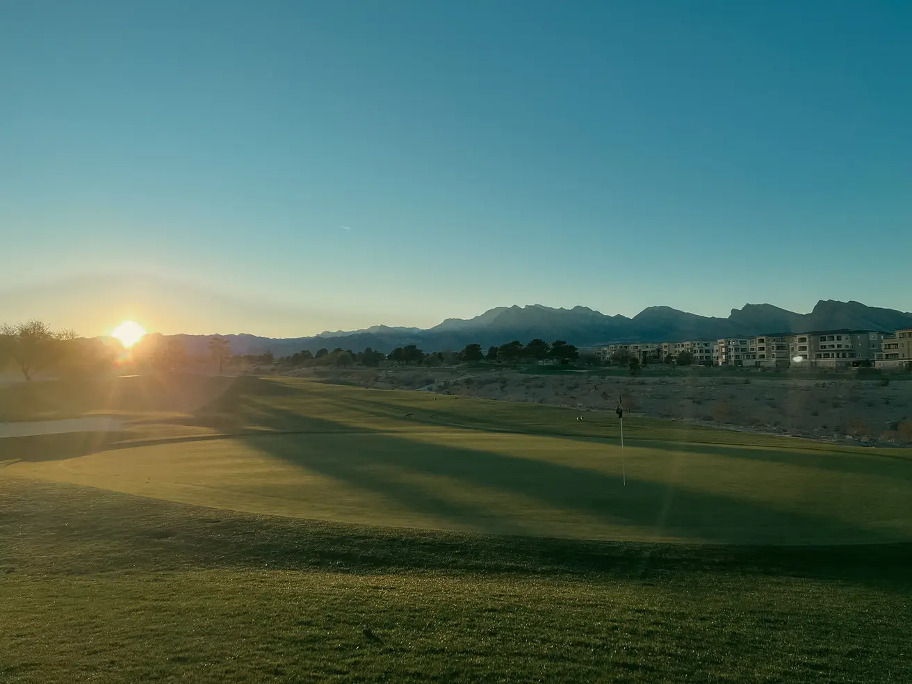 Sunset at Angel Park Golf Course with the putting green in the foreground and sun setting over the desert mountains in the distance