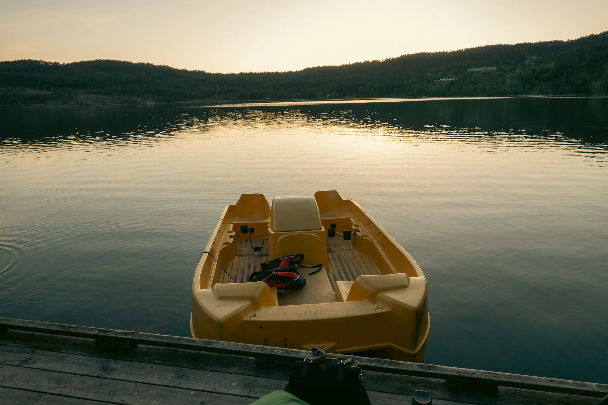 A paddleboat tied to the dock floating on the lake with mountains in the background at sunset.