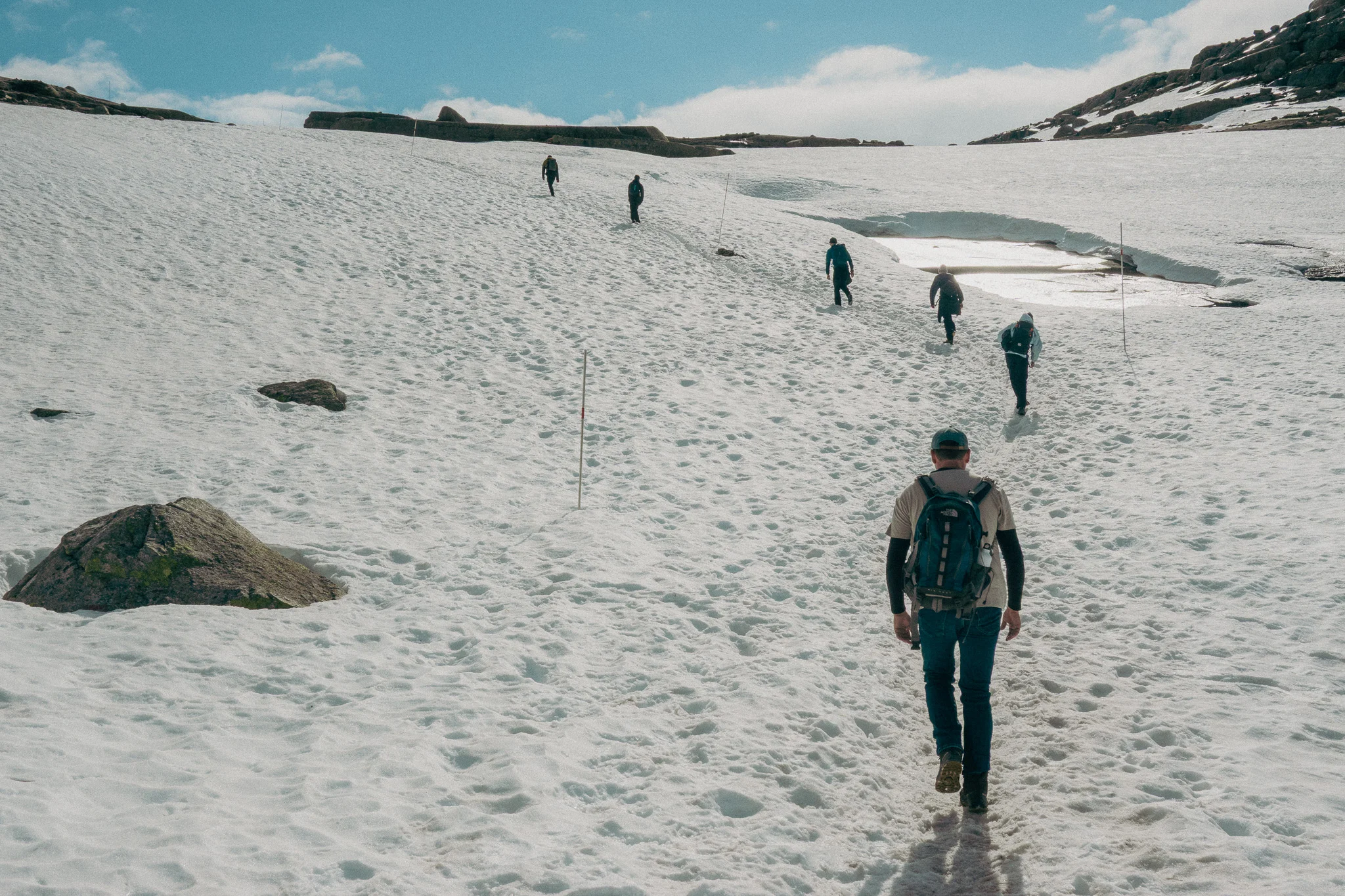 A line of adults hiking through snow surrounded by rocks and blue sky in the background on the Trolltunga trail in Norway