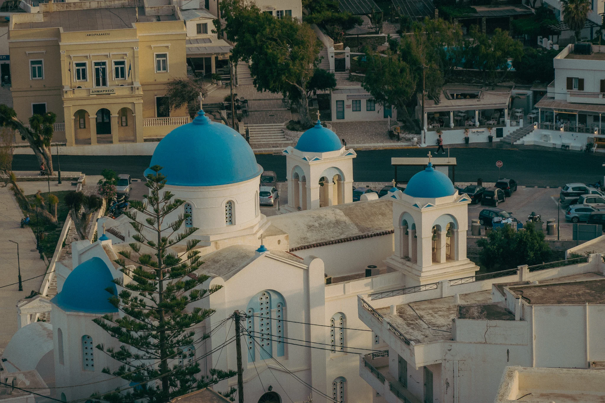 A white and blue chapel on the side of a hill with various buildings in the background
