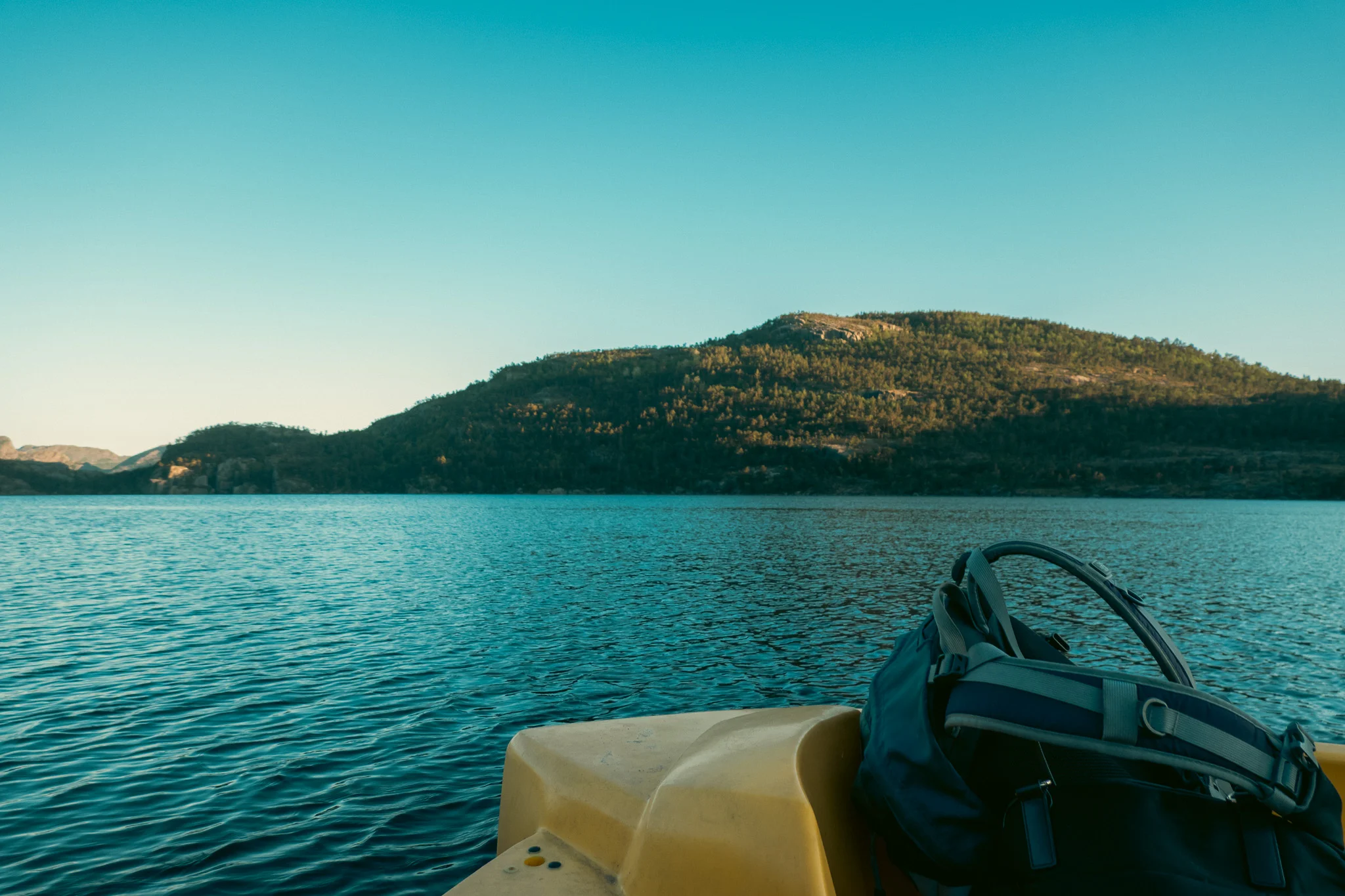 A backpack on the front of a paddle boat on a lake with a mountain in the background at sunset in Norway