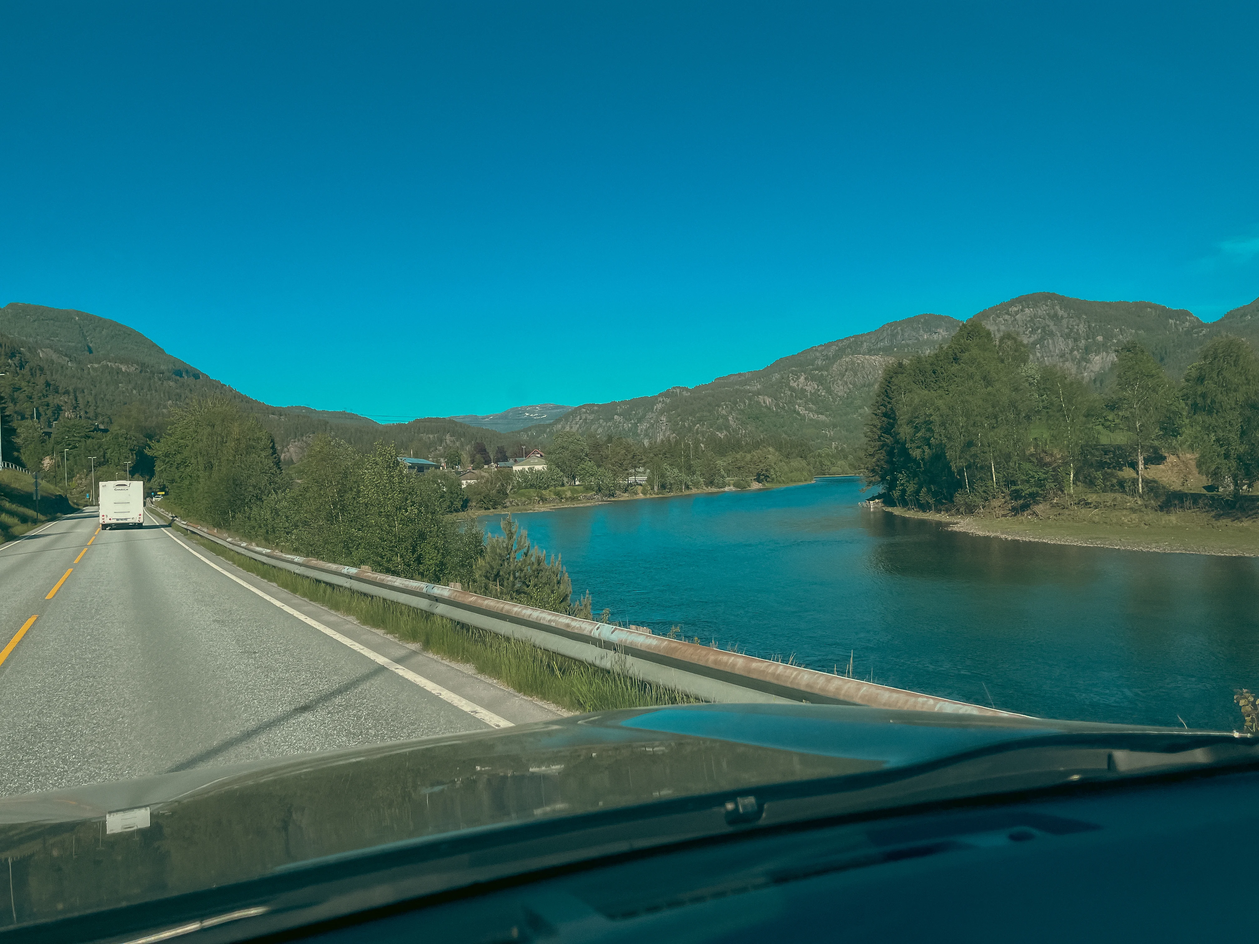 View from a car driving on a road alongside a tree-lined fjord.