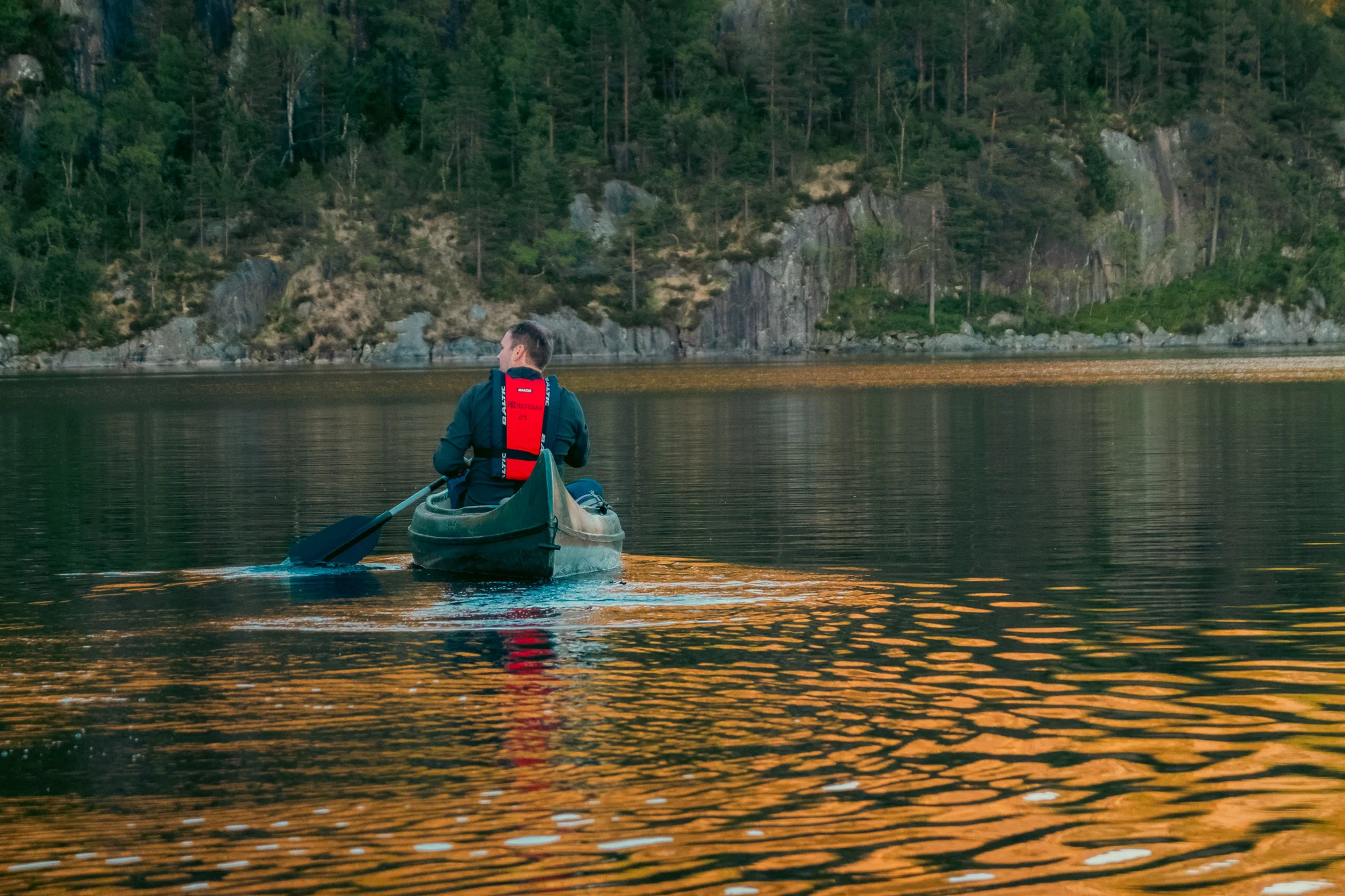 A man paddling a canoe on a lake with mountains in the background at sunset.