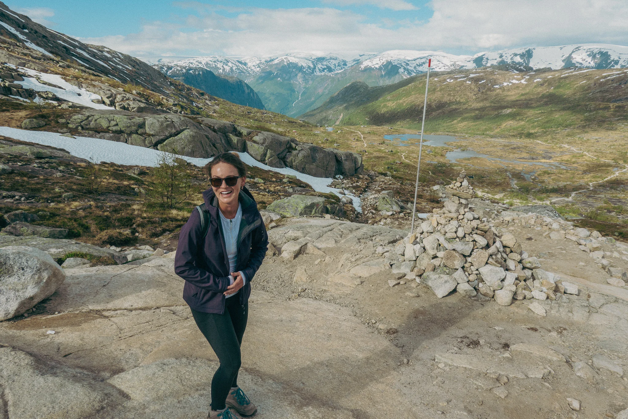 Adult female poses in front of scenic landscape and snowcapped mountains on the Trolltunga trail in Norway