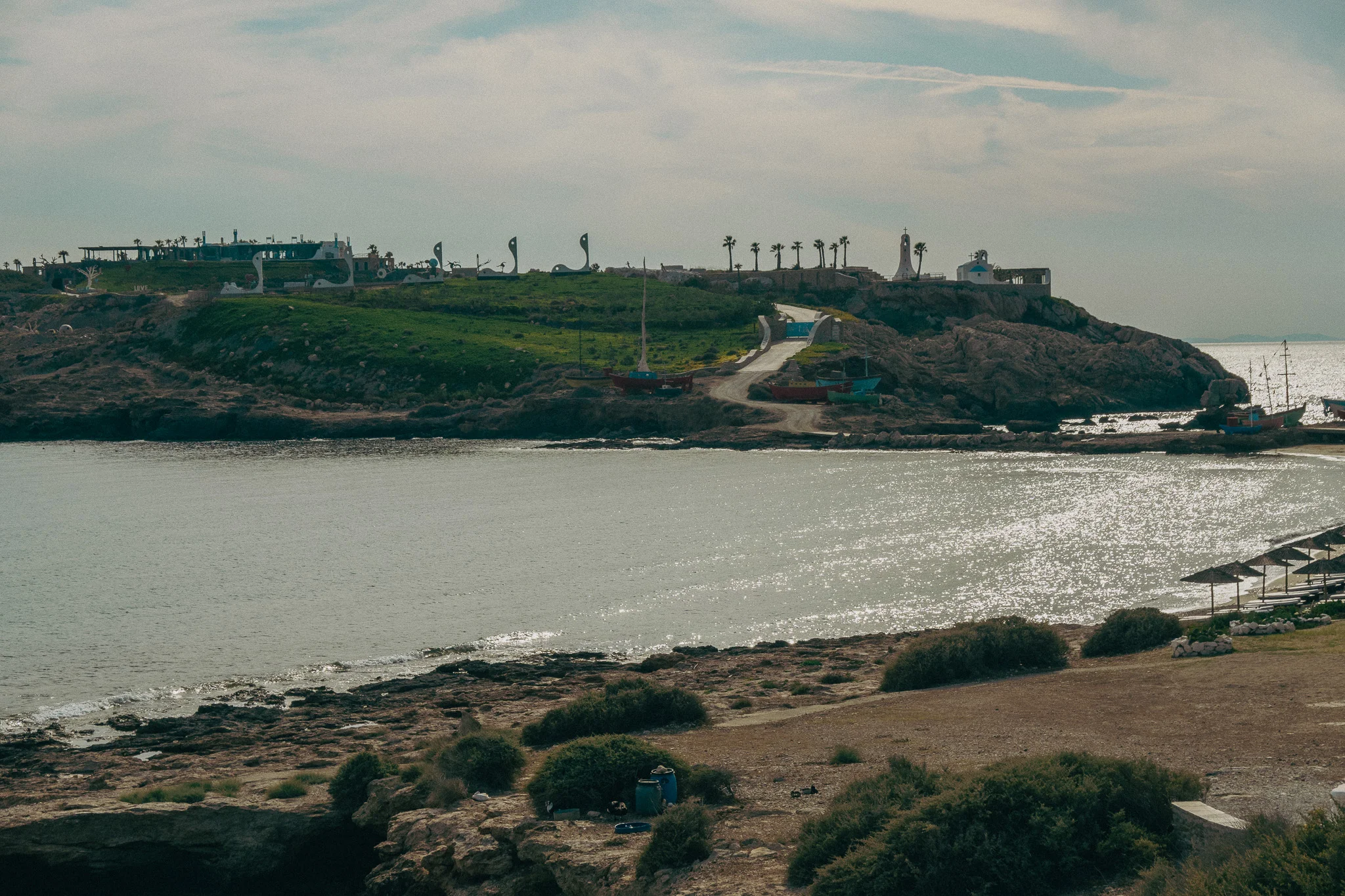 A small beach in the foreground with a green island with palm trees and buildings in the background