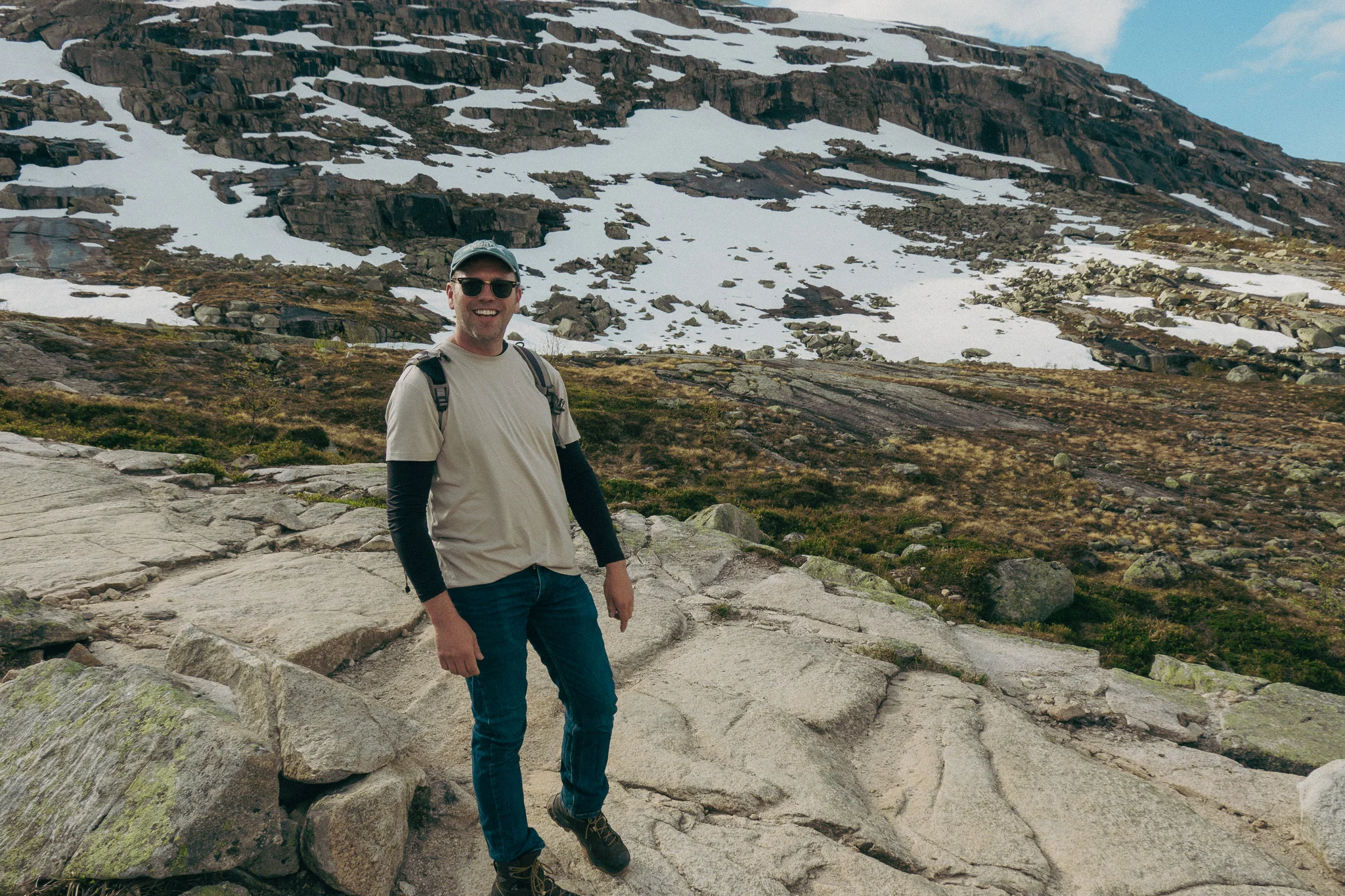 Adult male poses in front of scenic landscape and snowcapped mountains on the Trolltunga trail in Norway