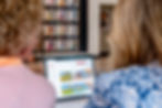 Two people viewed a laptop displaying property images. A colorful quilt of boots hangs on the wall in a cozy setting.