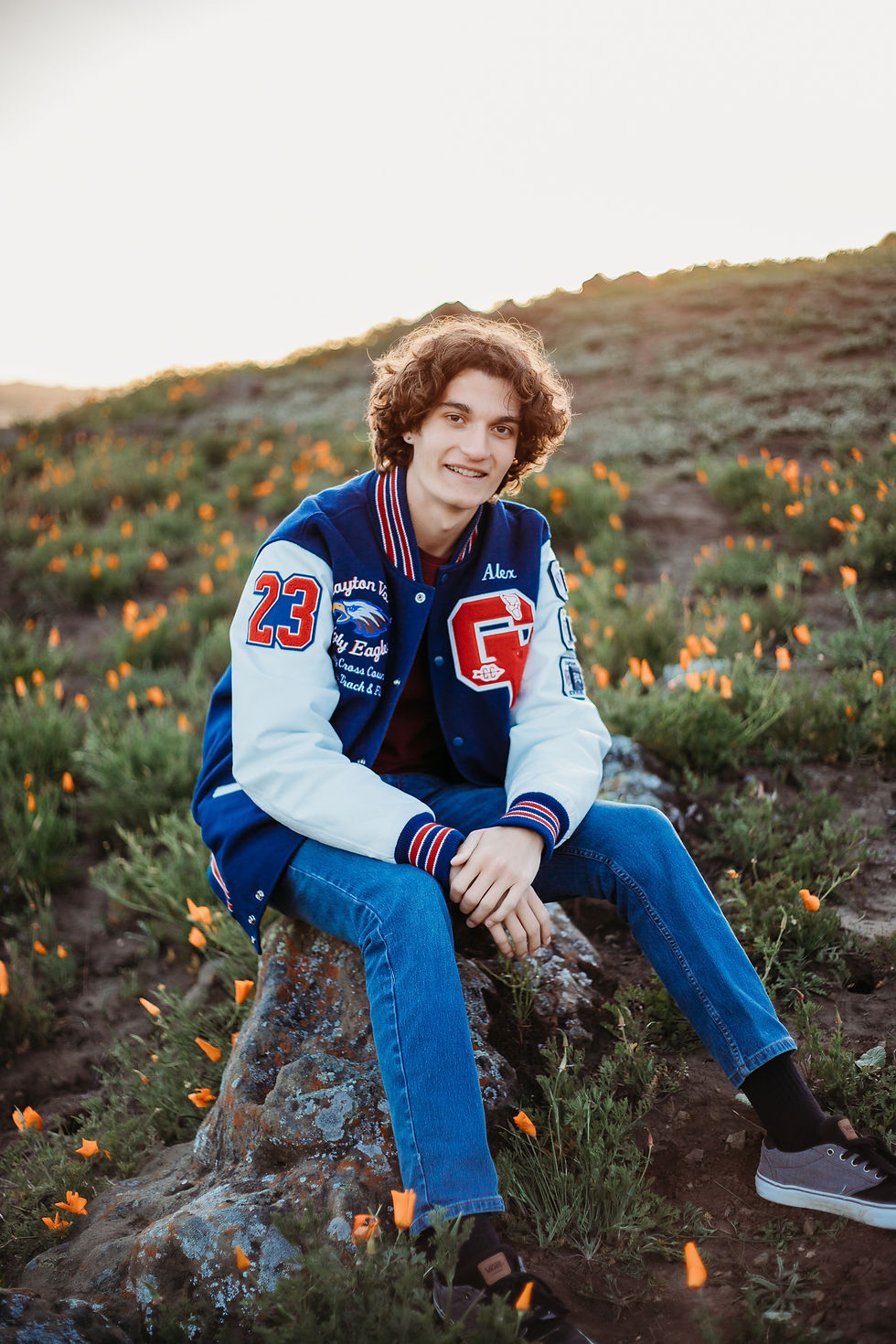 high school senior boy wearing letterman jacket in field of California poppies