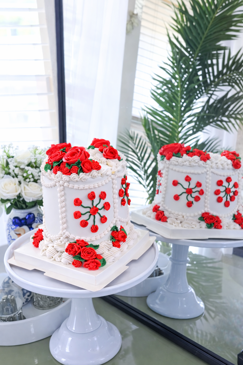 Two white cakes with red roses and decorative patterns