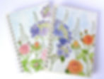 Two watercolour paintings covering notebooks: one with a field of blue and purple flowers, another with pink and red roses