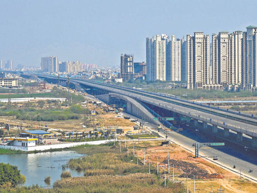 A modern construction site of a tertiary sewage treatment plant with tanks and pipelines, alongside the under-construction Sheetla Mata Devi Medical College in the background, showcasing civic infrastructure development in Gurgaon.