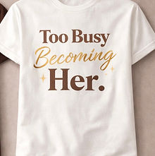 White t-shirt displaying "Too Busy Becoming Her." in brown and gold text.