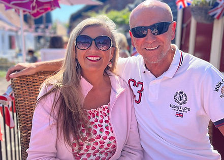 Smiling couple sitting at an outdoor café on a sunny day, dressed in summery outfits with red and white colours. The woman is