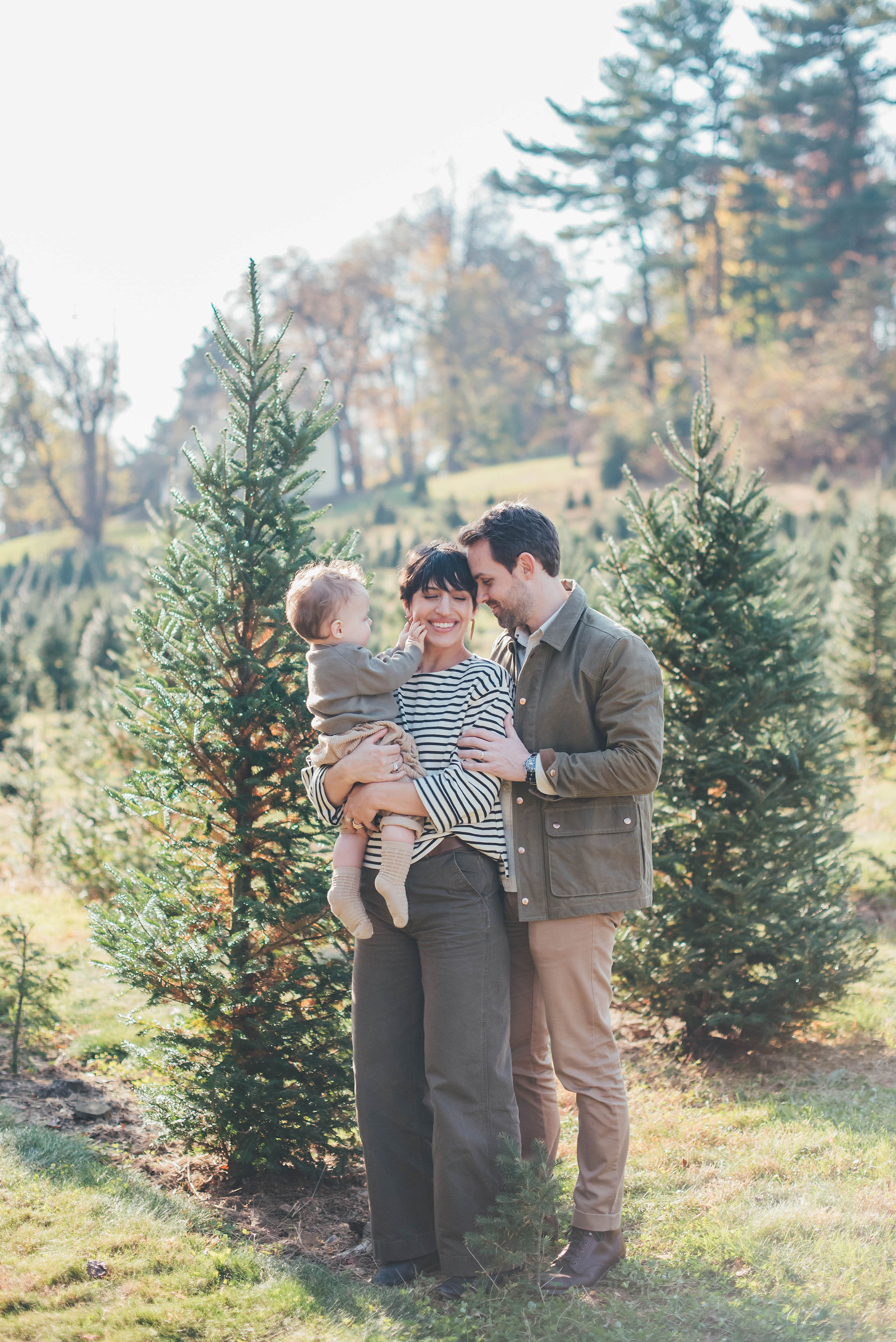 family of three in an embrace at a christmas tree farm