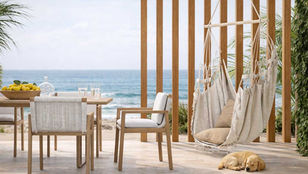 Coastal outdoor living space with wooden pergola, neutral lounge seating, hanging hammock chair, and ocean view, creating a calm, resort-like atmosphere.