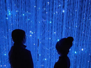 Two children are immersed in an ethereal mirrored room filled with hanging crystals with 1000's of multi coloured lights in teamlab Borderless Japan