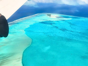 A plane flies over incredible blue islands and sand bars with striking blue water. Picture perfect Aitutaki Lagoon from the air, Cook Islands