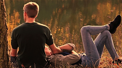 A couple in the grass together sitting by a tree